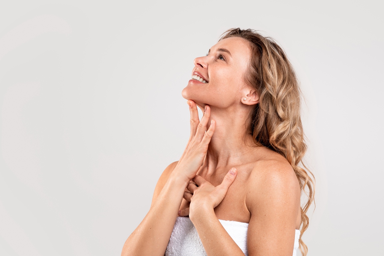 Mulher adulta olhando para cima com as mãos posicionadas perto do pescoço mostrando os efeitos de uma ritidoplastia completa cervicofacial. Mulher adulta olhando para cima com as mãos posicionadas perto do pescoço mostrando os efeitos de uma ritidoplastia completa cervicofacial.